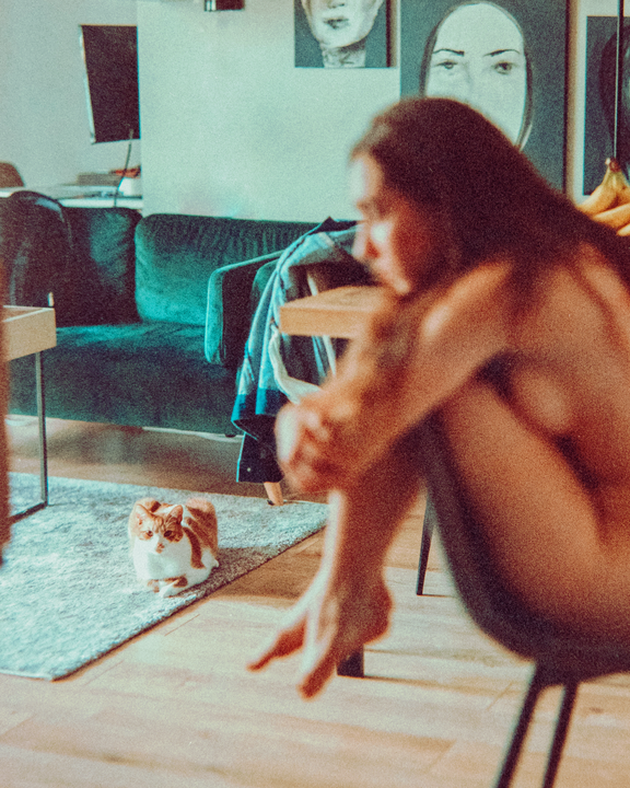 A woman sits on a chair in a room with a cat on the rug.