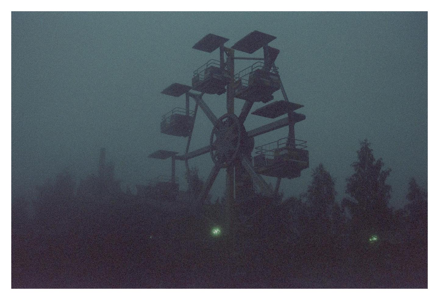 A ferris wheel stands tall amidst a hazy, dark landscape with trees.
