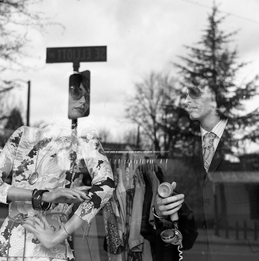 A man holds a telephone receiver while looking at a mannequin in a shop window.