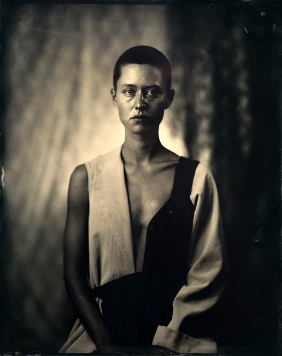 A woman with short hair wears a two-toned garment in a studio portrait.