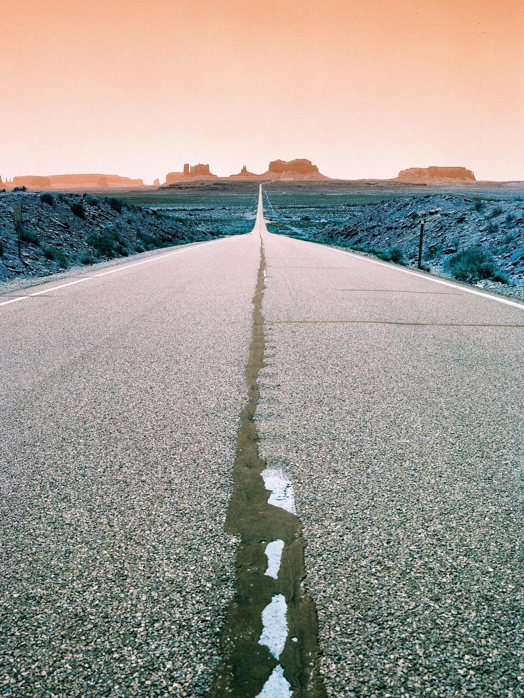 A long, straight road leads to distant rock formations under an orange sky.