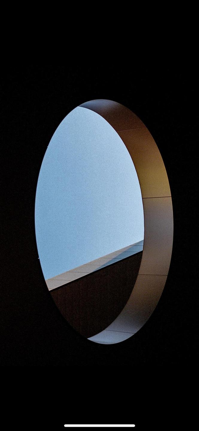 A circular window reveals a bright blue sky and a building with a dark roof.