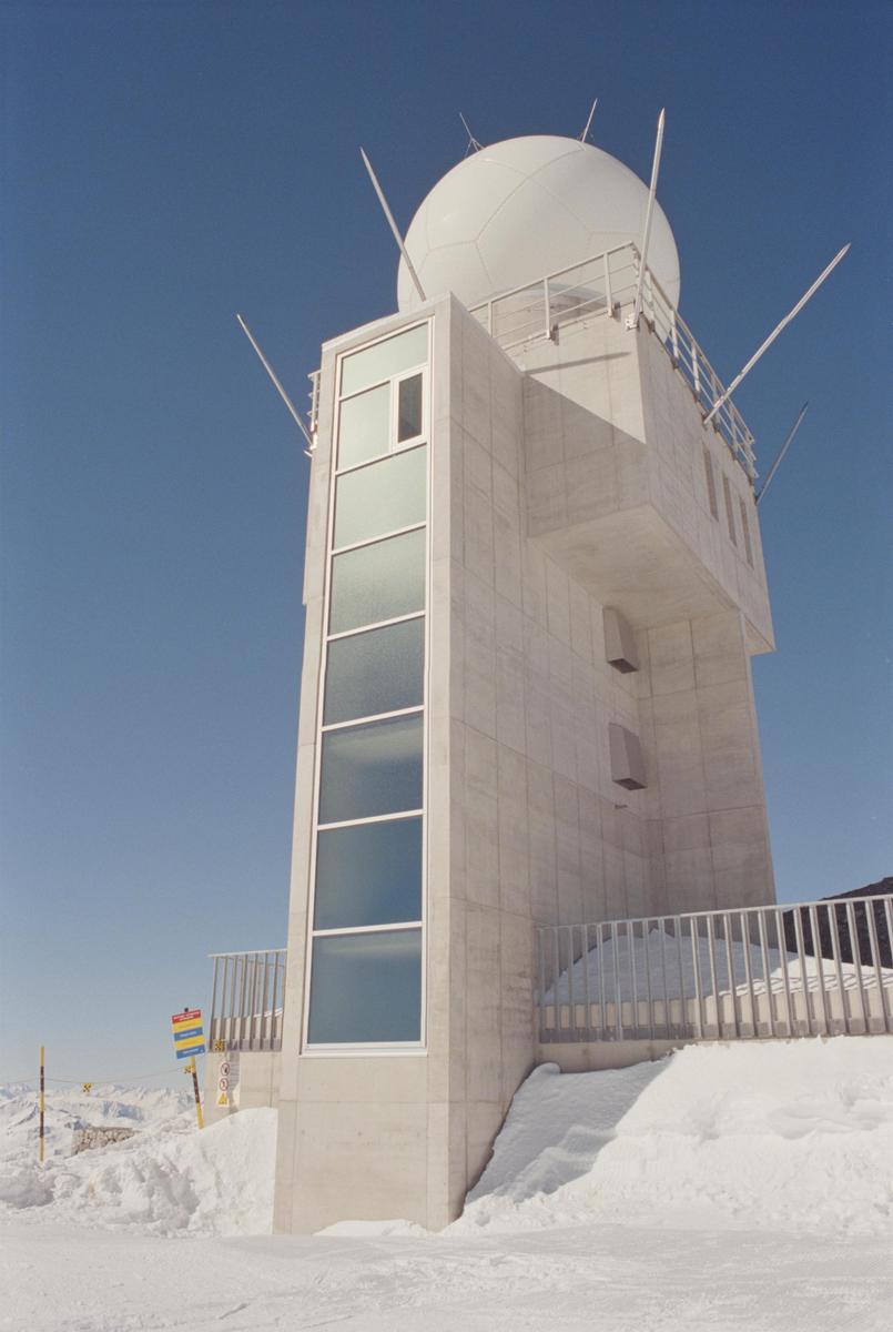 A meteorological observatory with a large white dome on top stands in a snowy landscape under a clear blue sky.