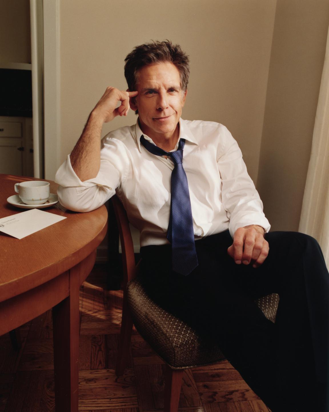 A man in a white shirt and blue tie sits at a wooden table with a cup and envelope.