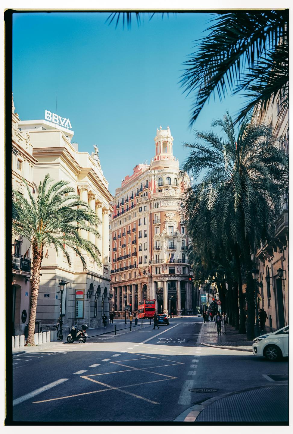 A street in Valencia is lined with palm trees and historic buildings under a clear blue sky.