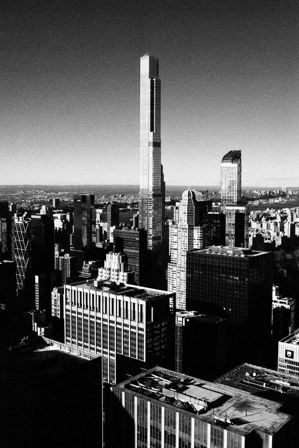 An aerial view shows a dense urban landscape with numerous skyscrapers under a clear sky.
