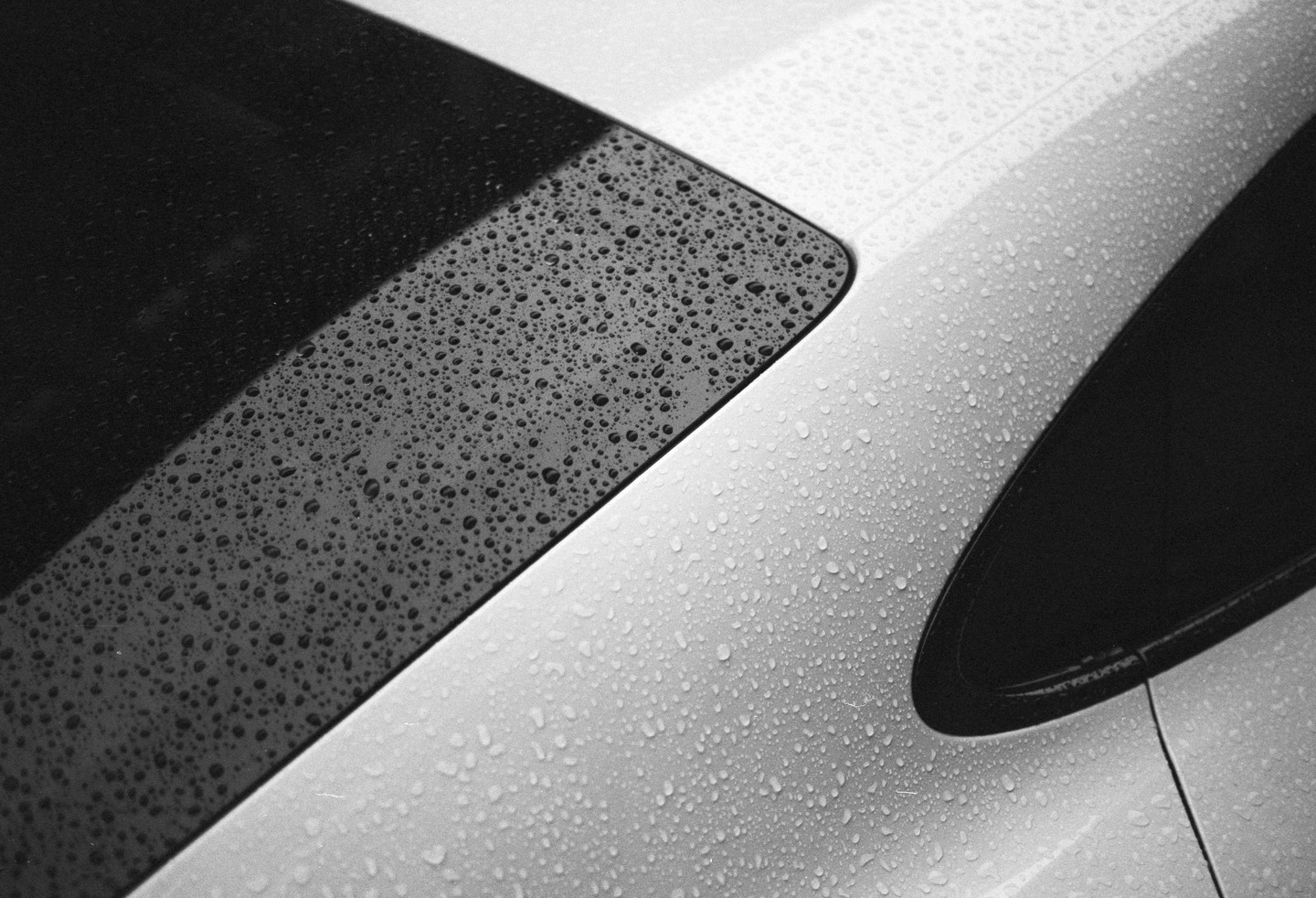 Raindrops cover the black and white surfaces of a vehicle.