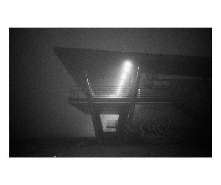 A building with a balcony and graffiti is shrouded in fog at night.