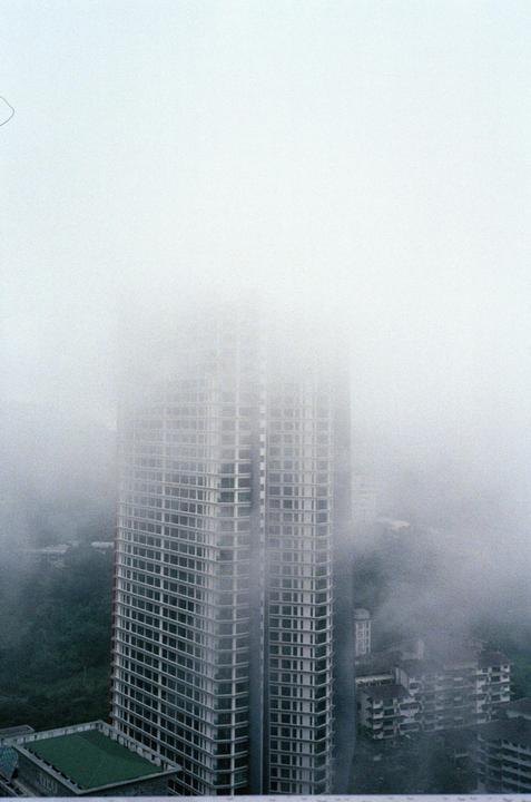 A tall building is partially obscured by fog, with other buildings and trees visible below.