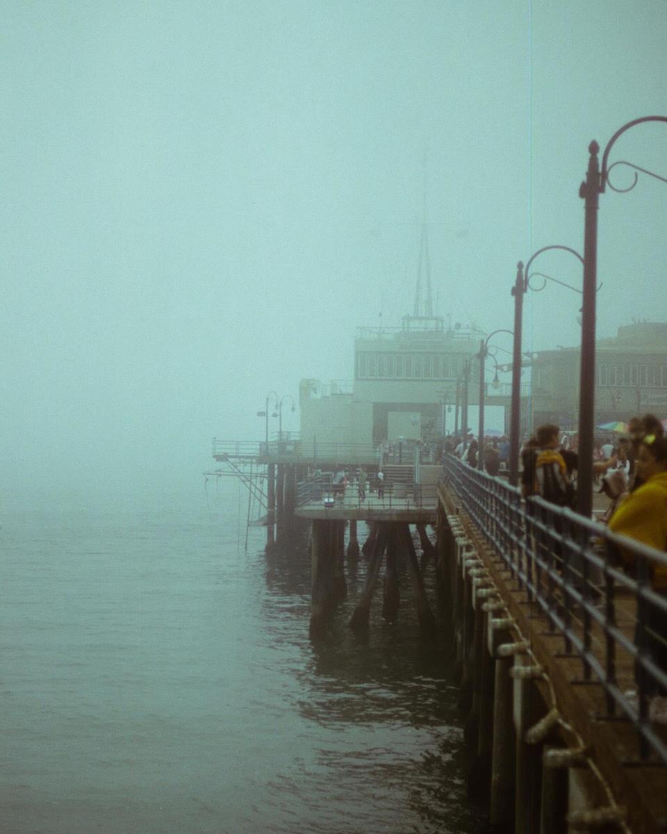 A pier extends into a hazy body of water with buildings visible in the distance.