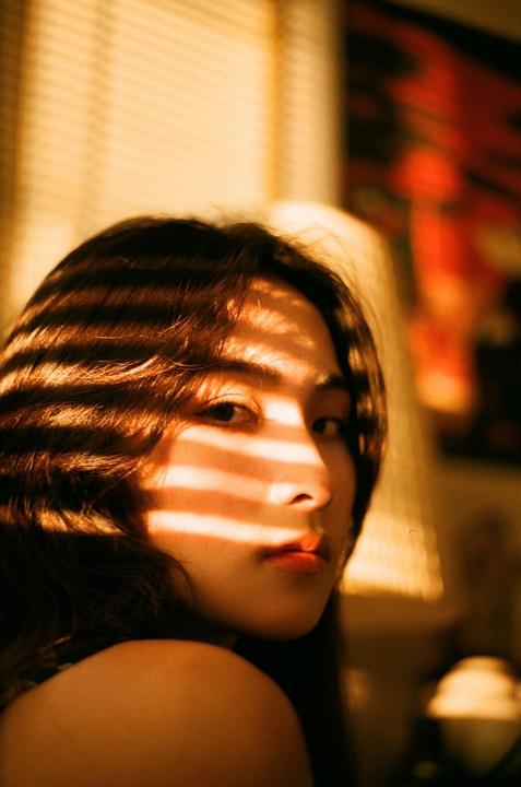 A woman with long hair looks over her shoulder, with light and shadow stripes across her face.