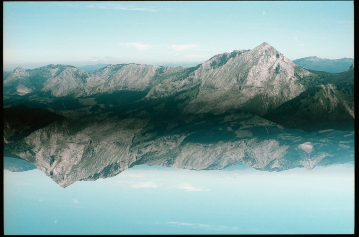 A double exposure shows a mountain range reflected upside down against a blue sky.