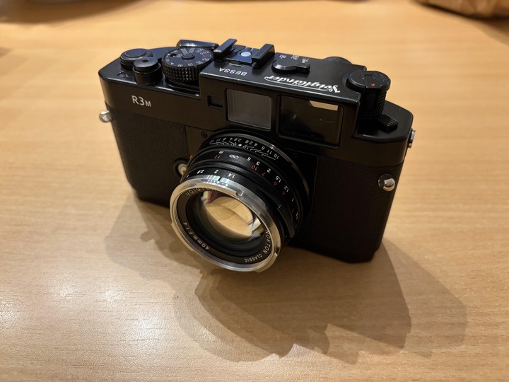 A black rangefinder camera with a silver lens sits on a wooden surface.
