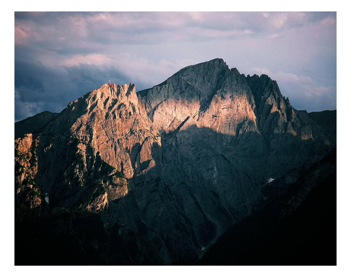 A mountain peak is illuminated by the setting sun under a cloudy sky.