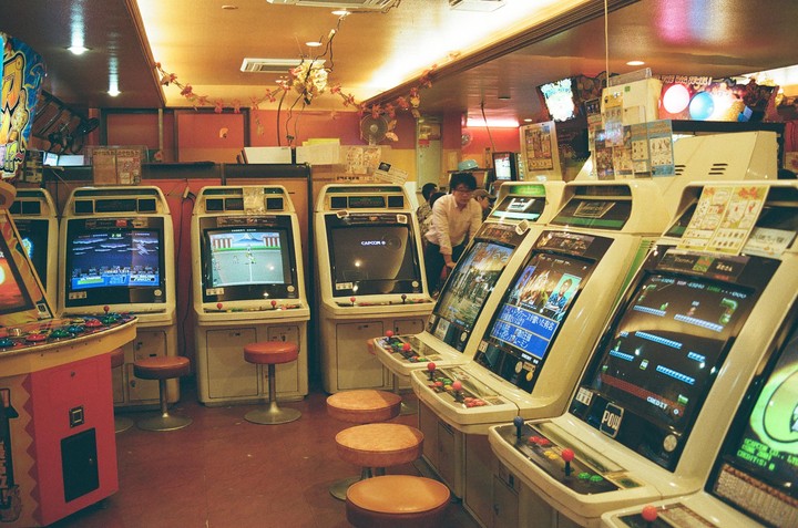 A man stands among rows of arcade machines in a brightly lit arcade.