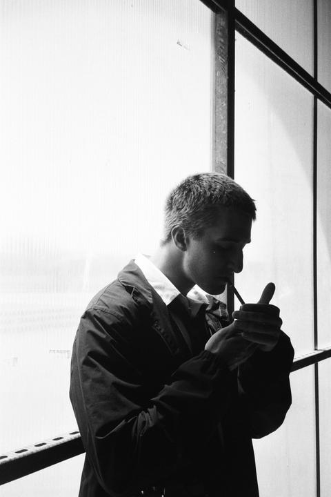 A man lights a cigarette in front of a window.