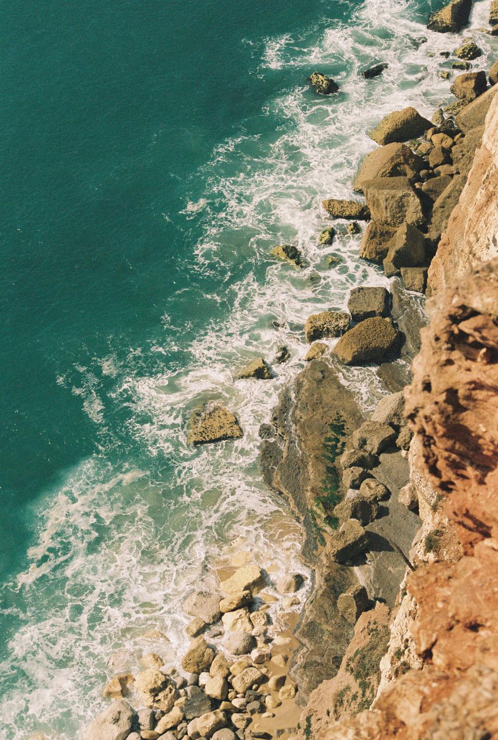 Waves crash against a rocky shore at the base of a cliff.