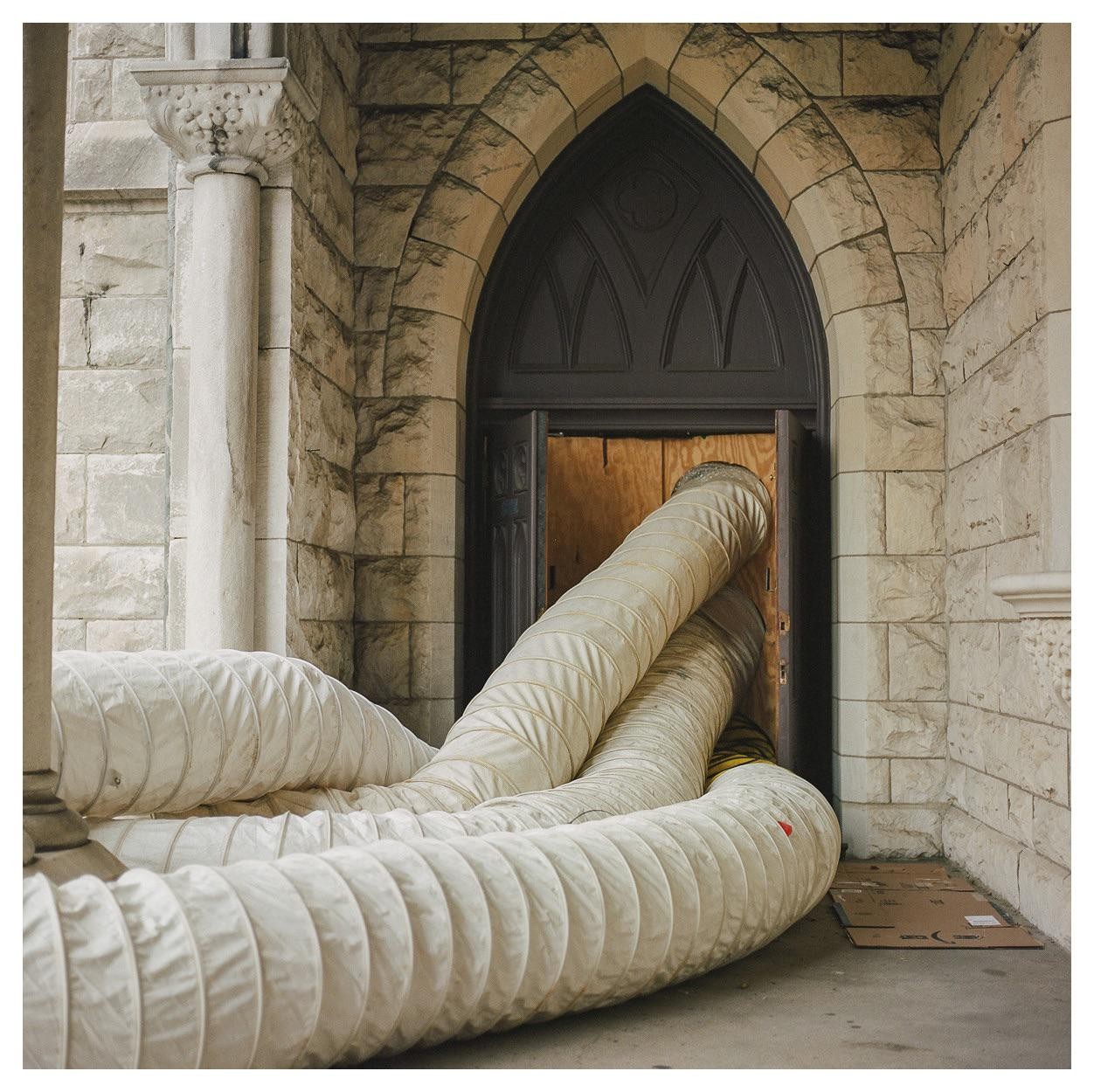 Two large white tubes extend from an open door in a stone building.