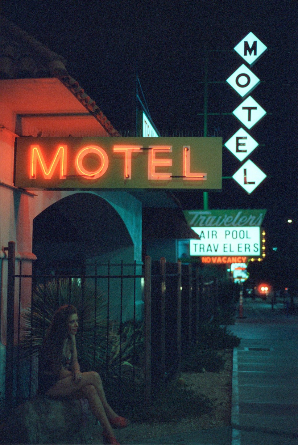 A woman sits on a rock next to a motel sign at night.