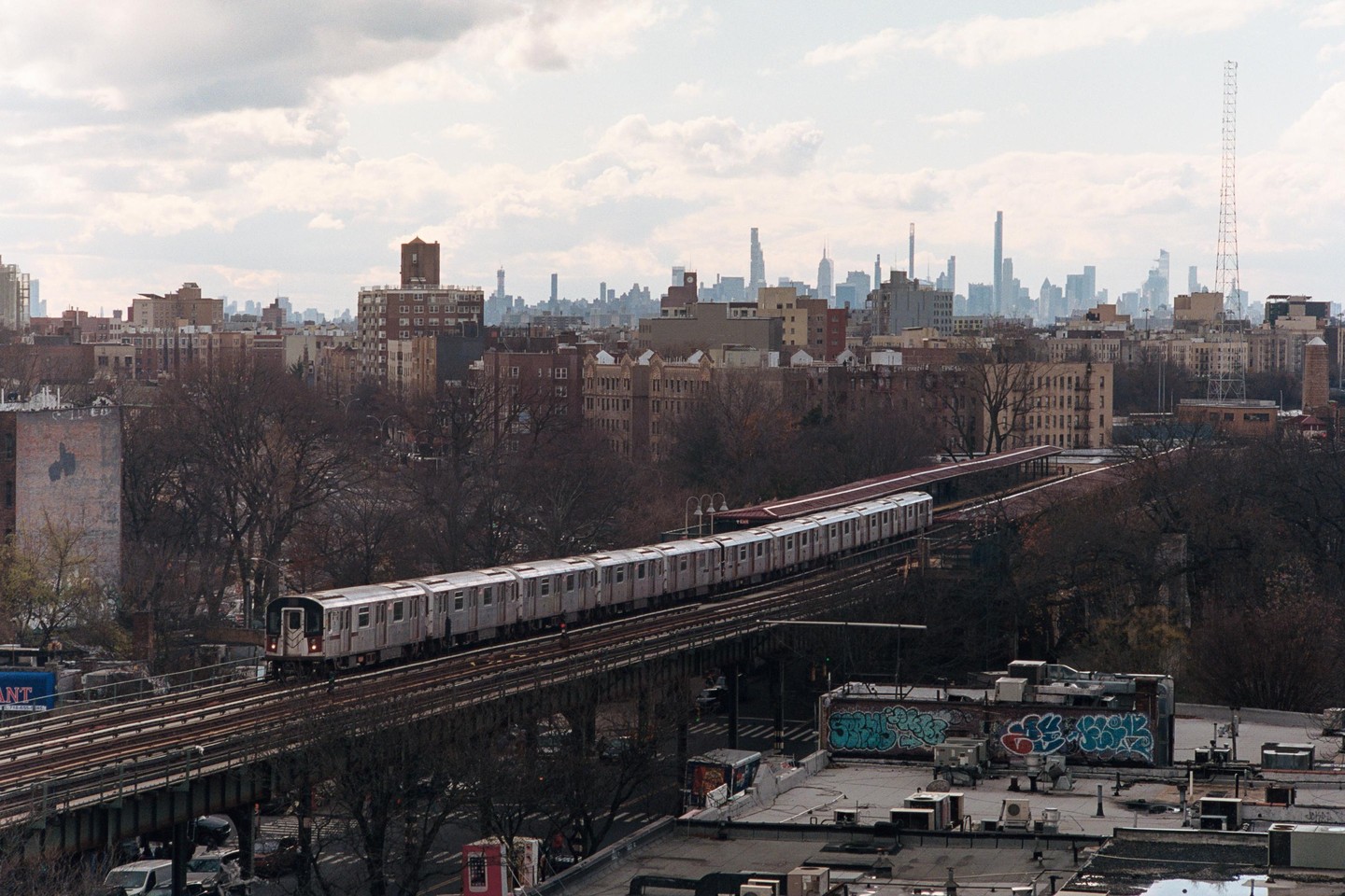 A subway train travels on an elevated track through a city with a skyline in the distance.