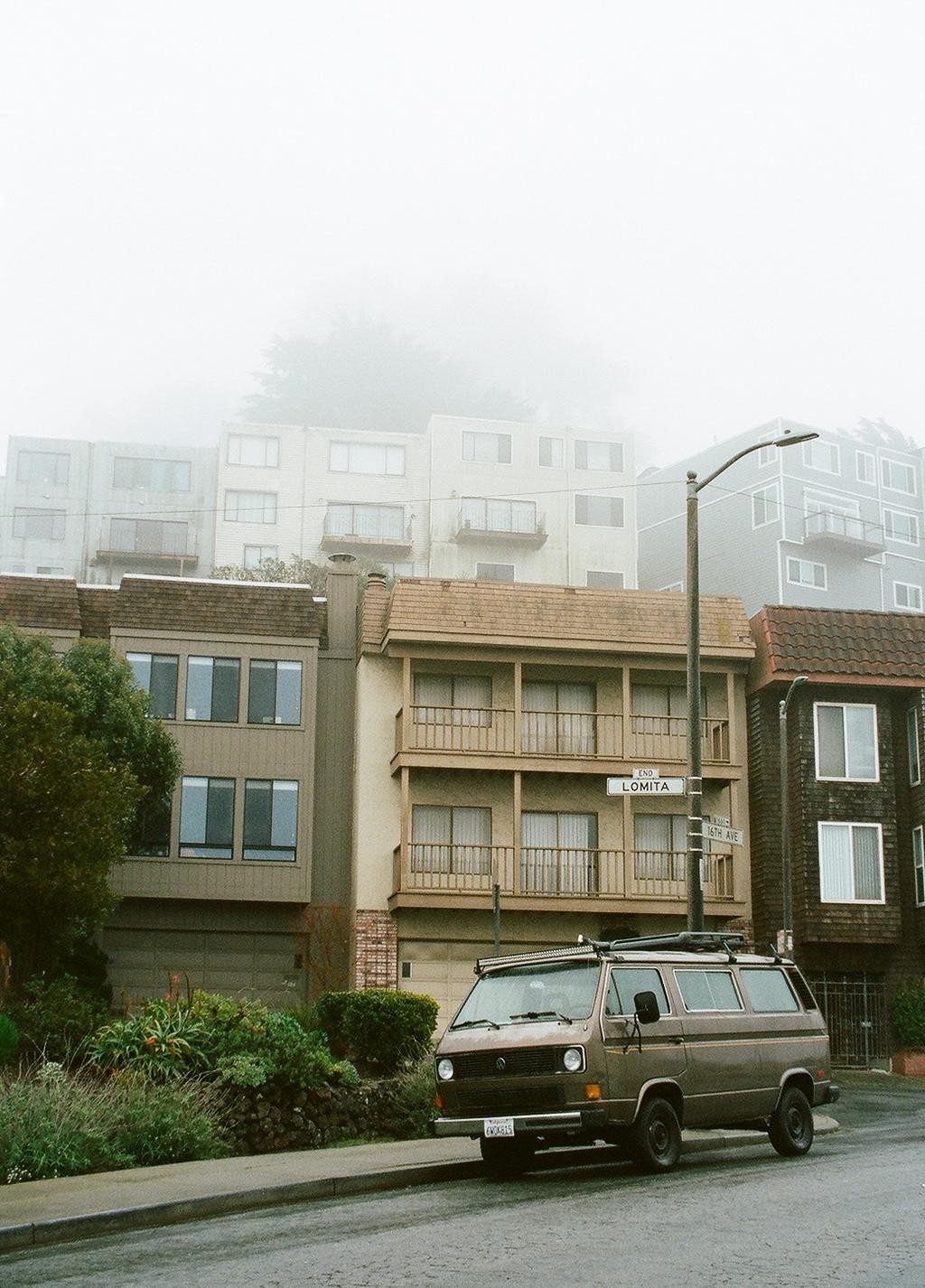 A brown van is parked on a street in front of buildings on a foggy day.