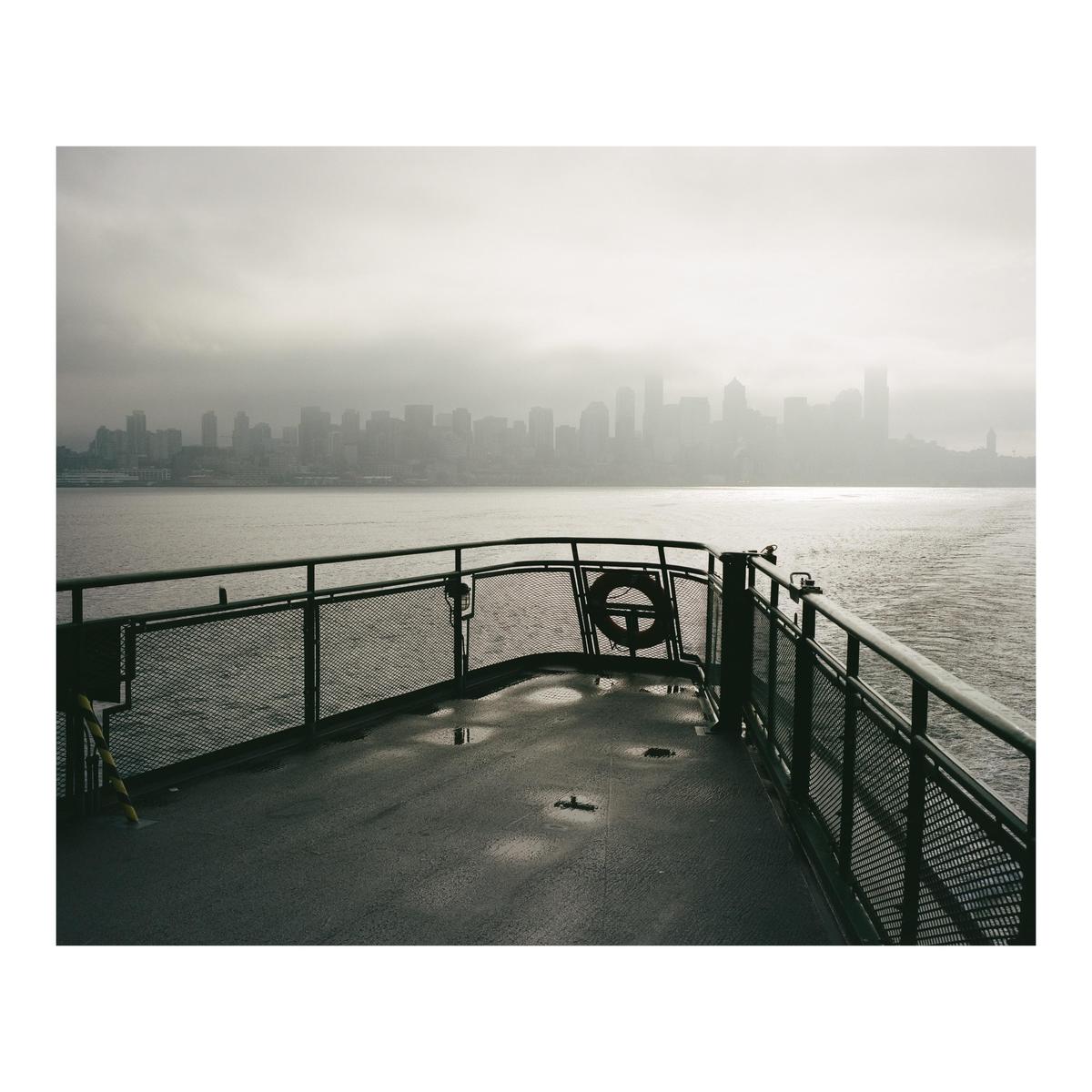 A ferry approaches a hazy city skyline across a body of water.