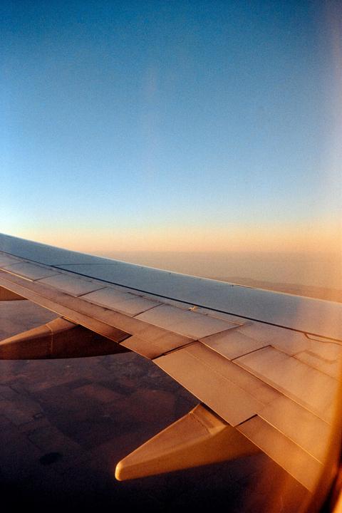 An airplane wing is visible against a clear sky and distant land during descent.