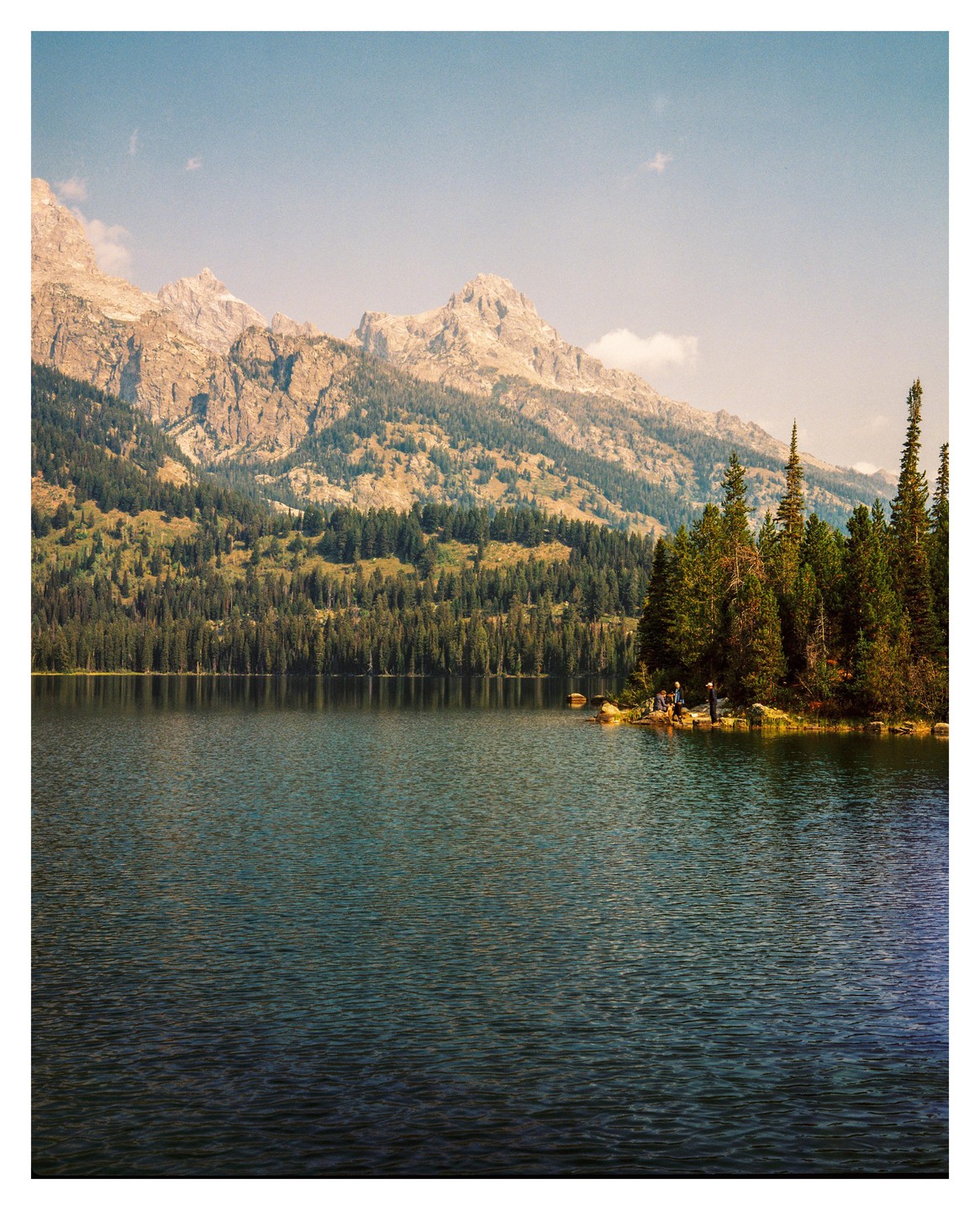 A lake is surrounded by a forest and mountains under a clear sky.