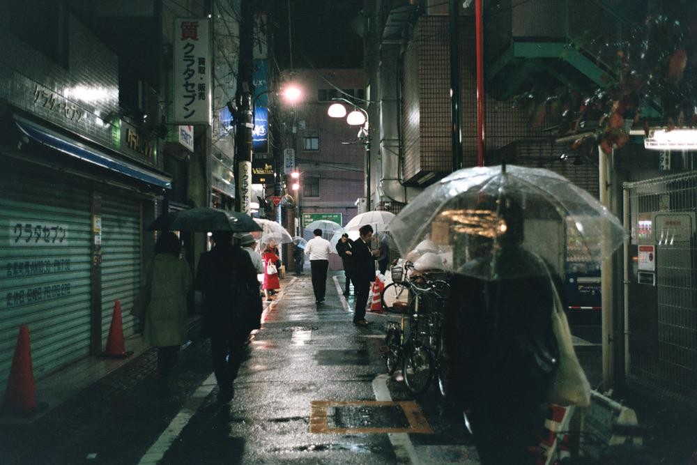 People walk with umbrellas on a wet street at night in Tokyo.