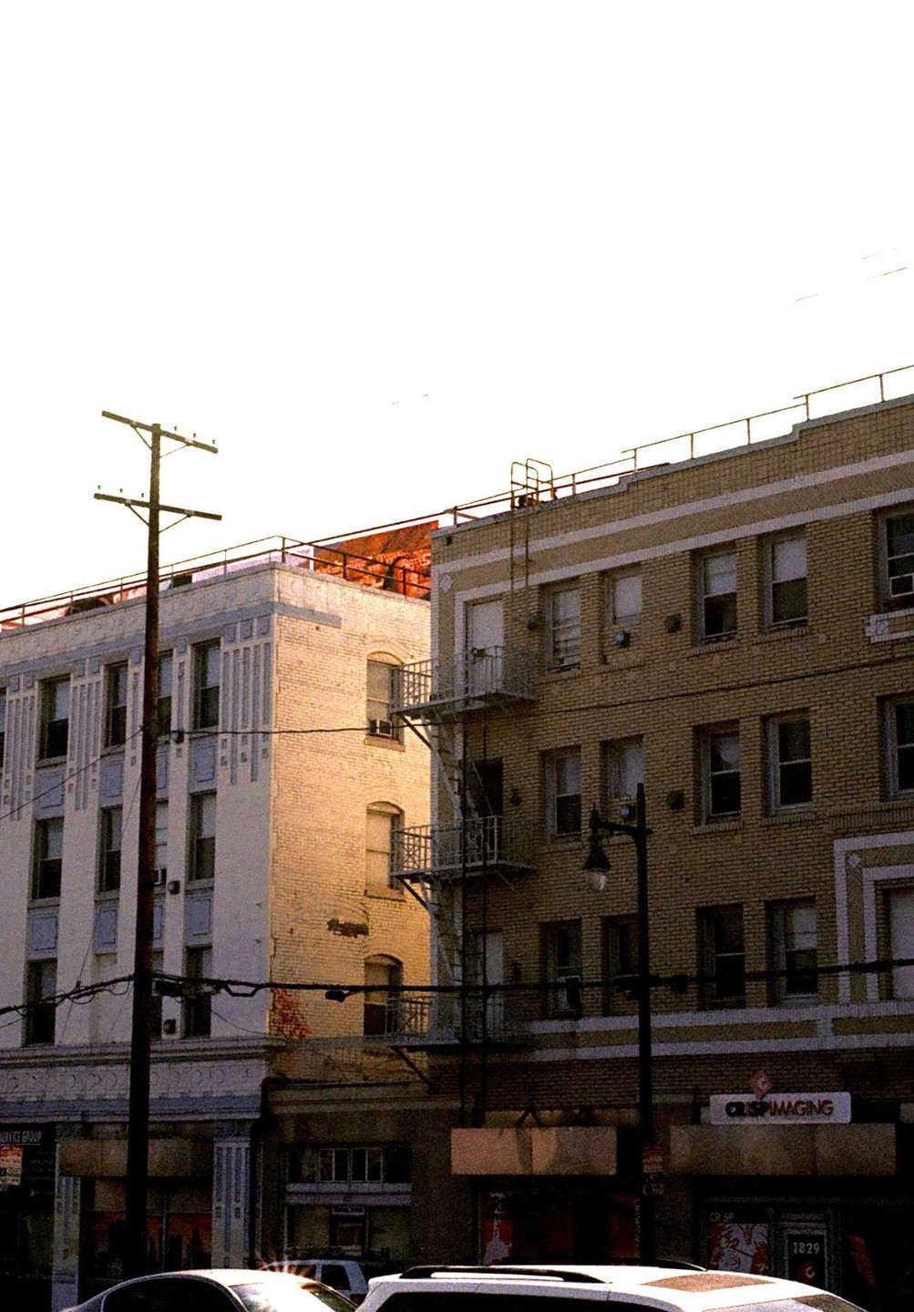 Two buildings with fire escapes and a utility pole stand under a bright sky.