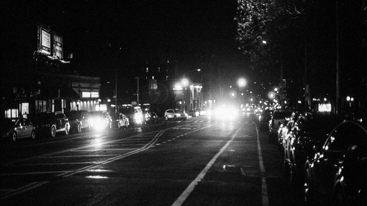 A street in Washington Heights is filled with cars and bright lights at night.