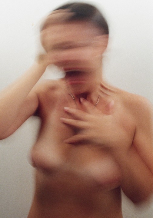 A blurry self-portrait shows a woman with her hands near her face and chest.