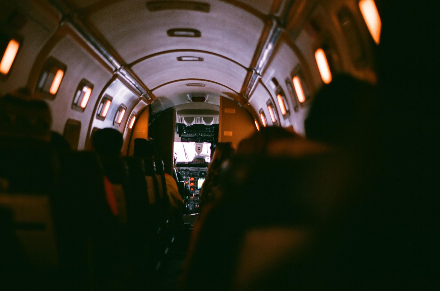 The interior of a small airplane is visible from the perspective of a passenger looking towards the cockpit.
