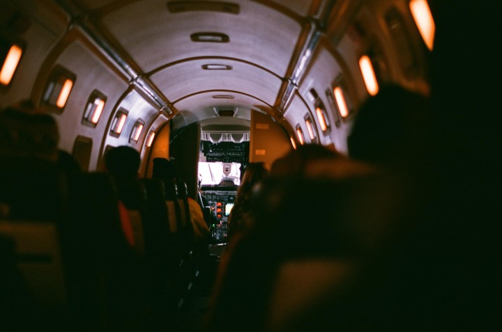 The interior of a small airplane is visible from the perspective of a passenger looking towards the cockpit.