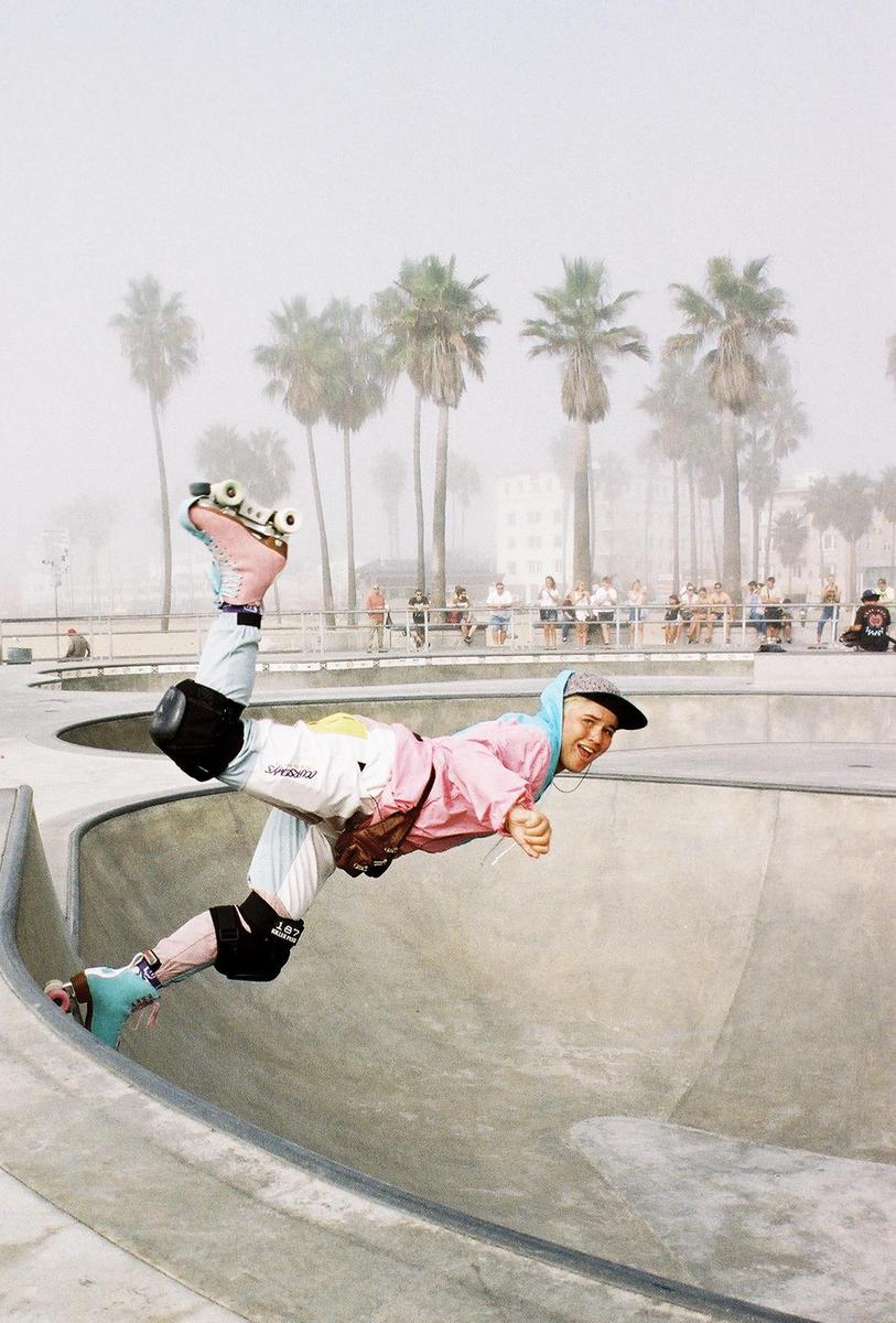 A person on roller skates is in mid-air in a skate park with palm trees in the background.