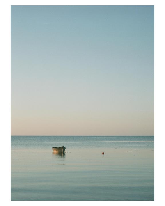A small boat floats on calm water under a clear sky.