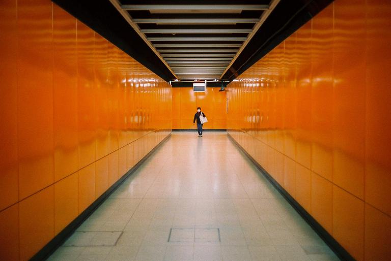 A person walks down a long, narrow, orange-walled corridor.