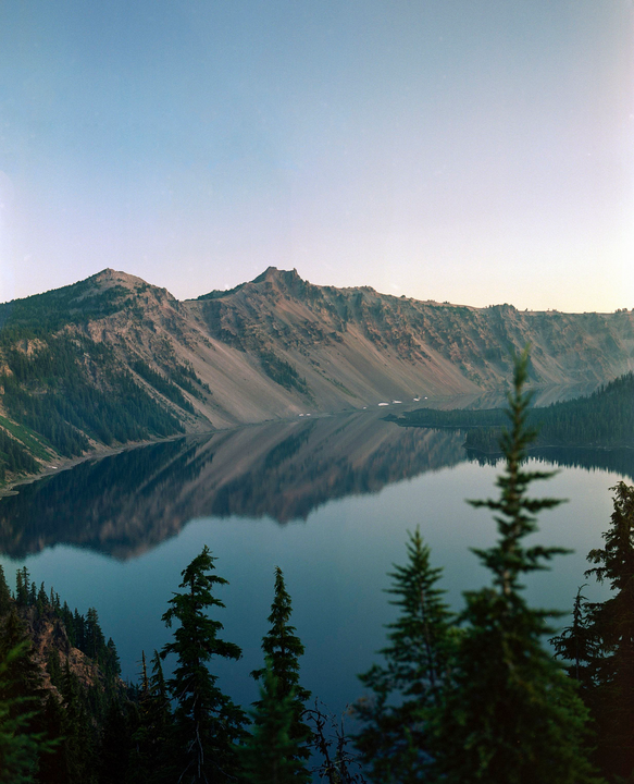 A large lake reflects the mountains and sky, with evergreen trees in the foreground.