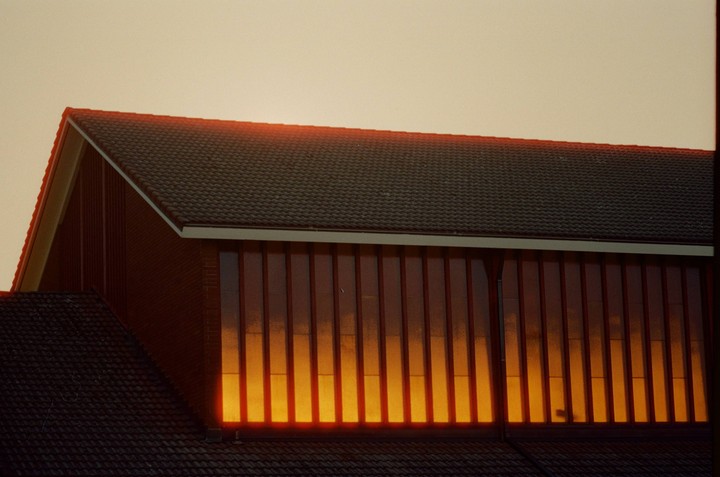 The windows of a building reflect a bright orange light, contrasting with the dark roof tiles.