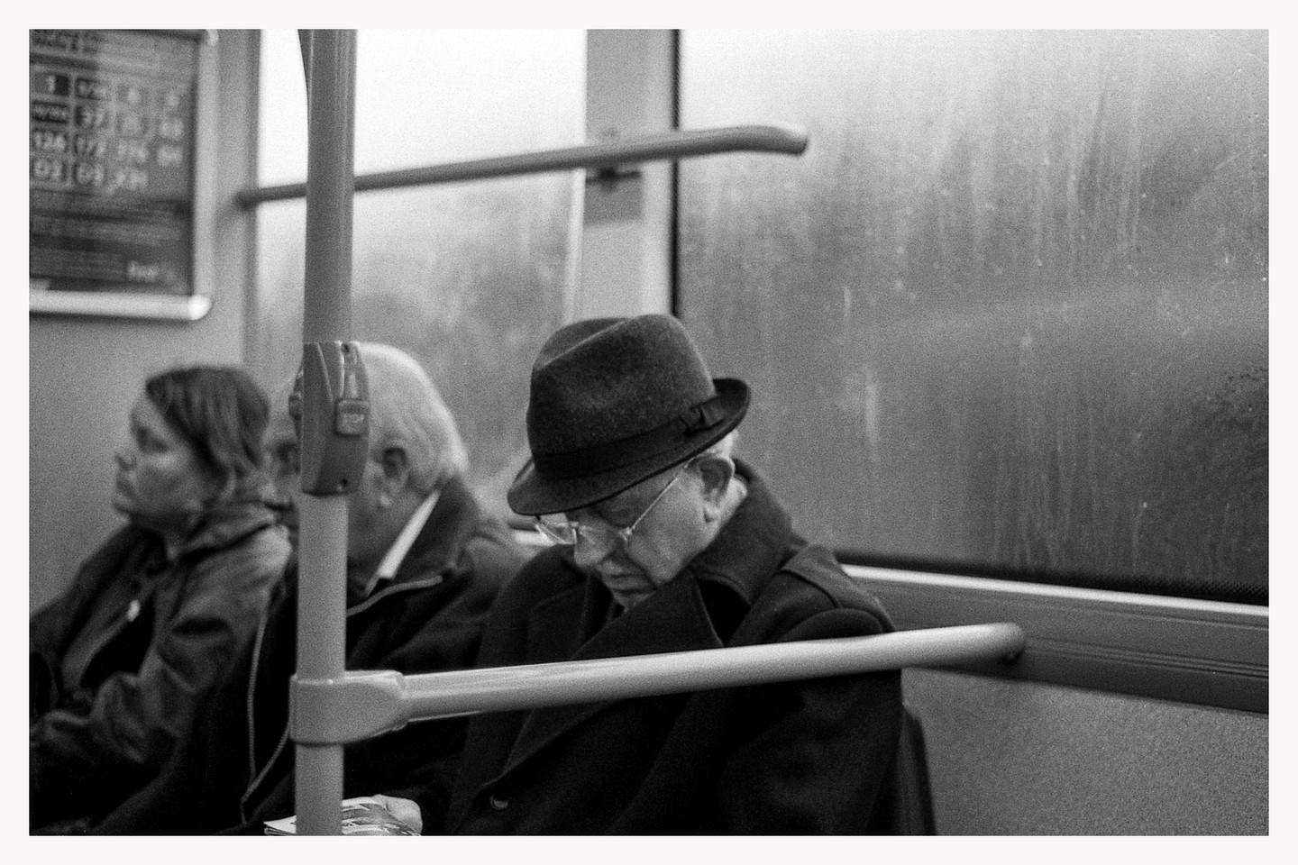 A man in a fedora sleeps on a bus next to other passengers.