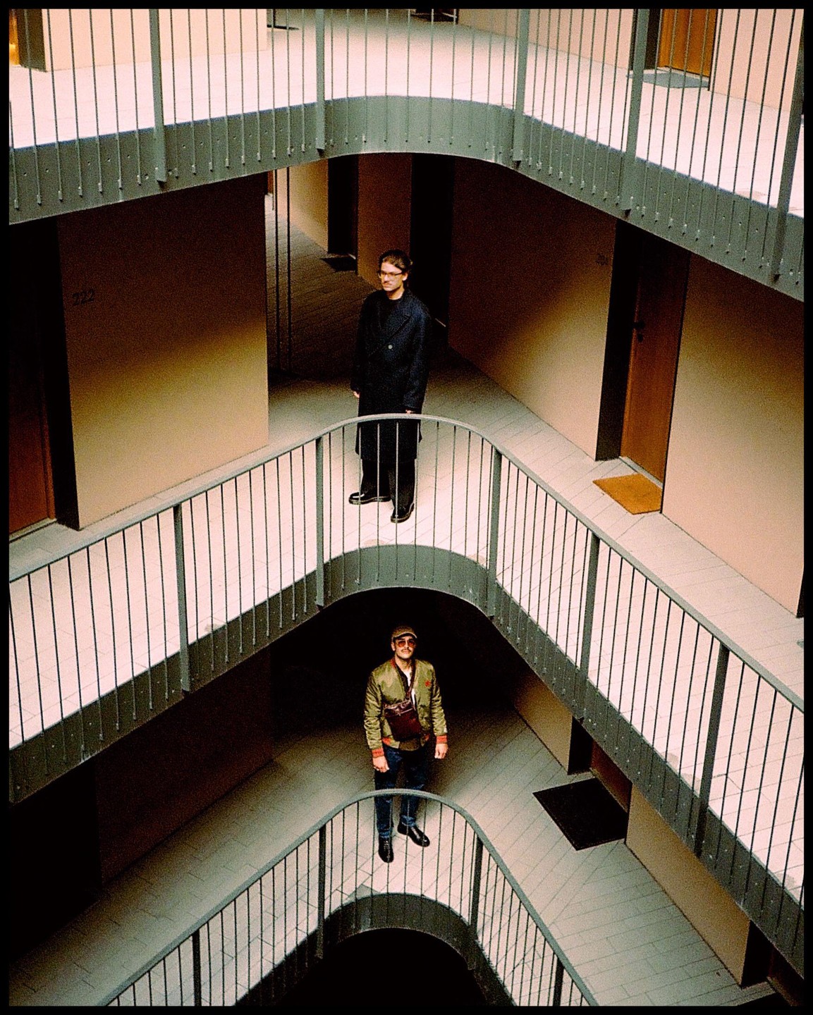 Two men stand on different levels of a building with curved hallways and railings.