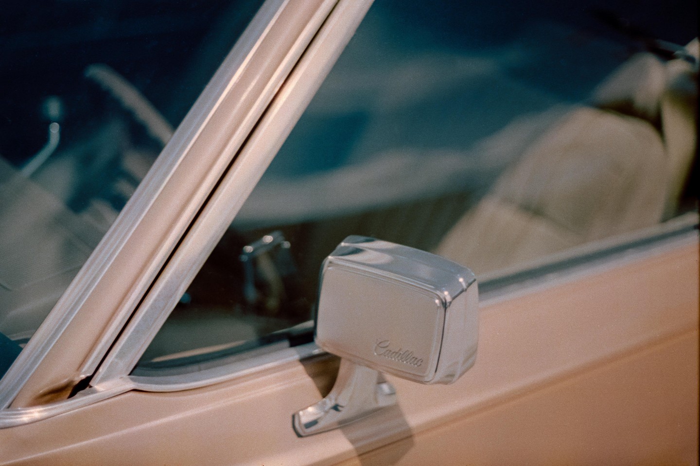A chrome Cadillac side mirror is visible on a beige car.