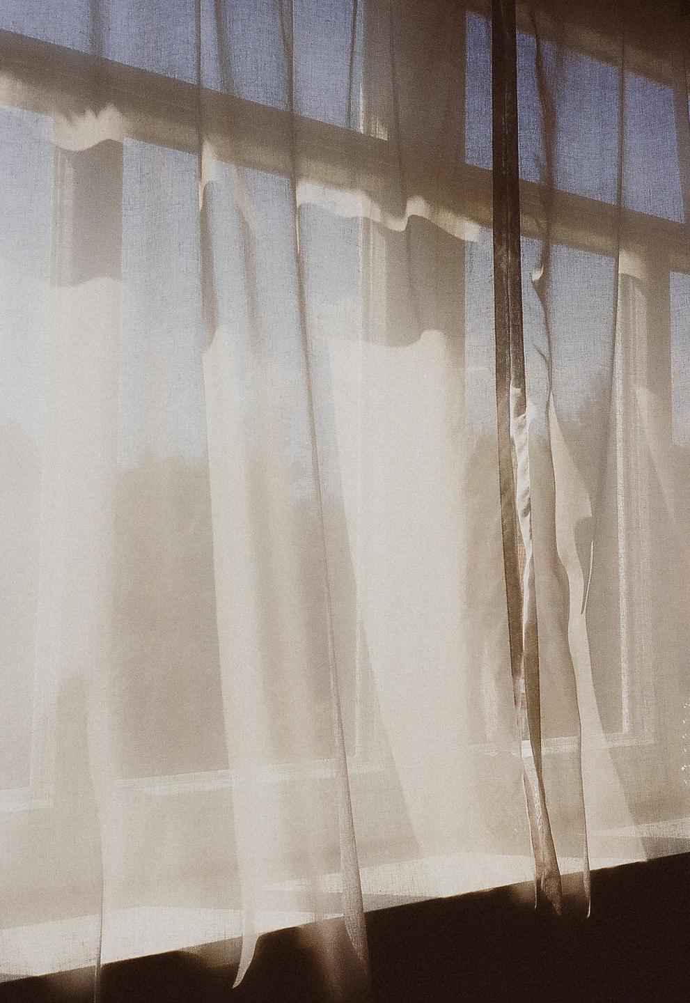 Sunlight streams through sheer white curtains covering a window.