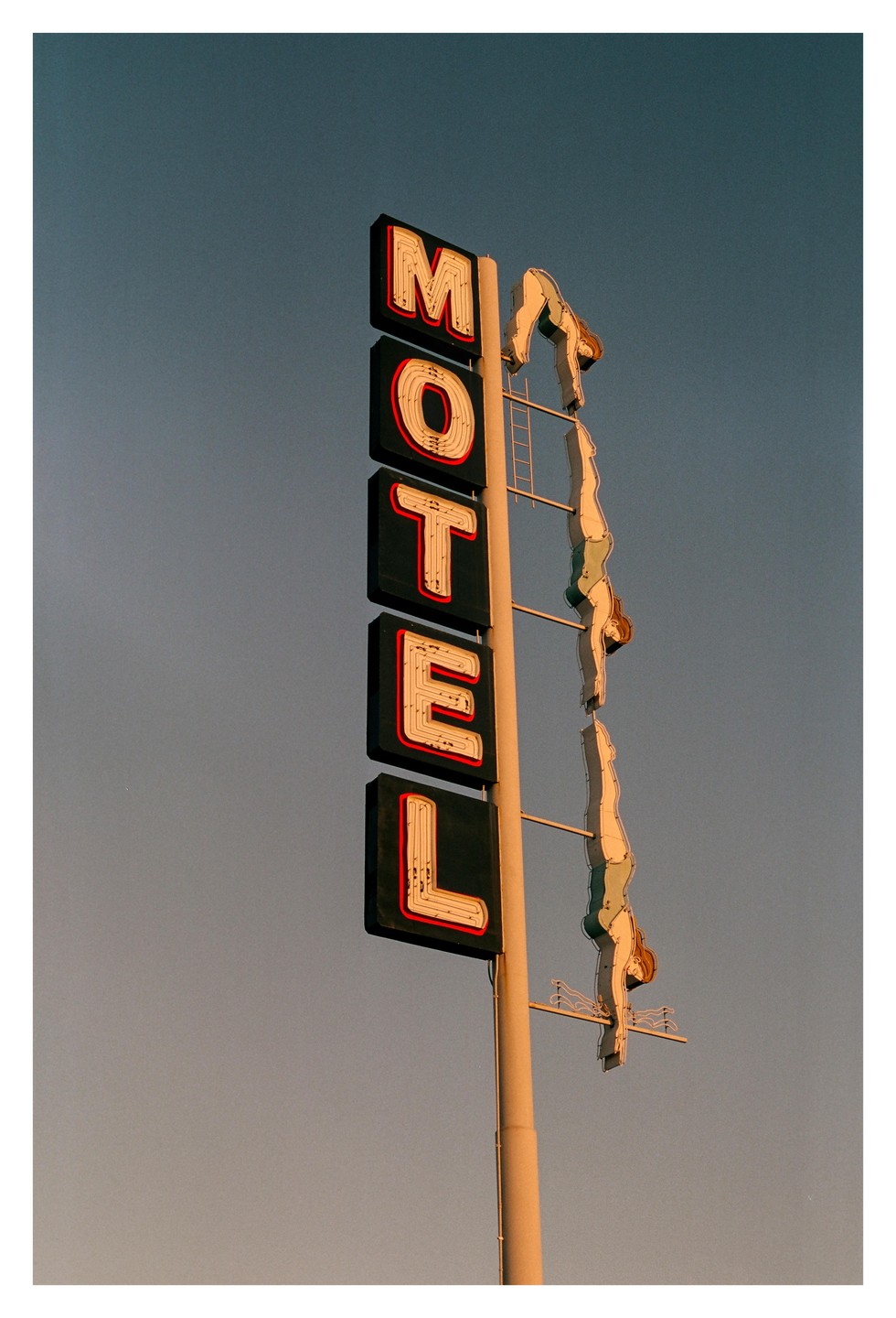 A neon motel sign with a diving woman is set against a clear sky.