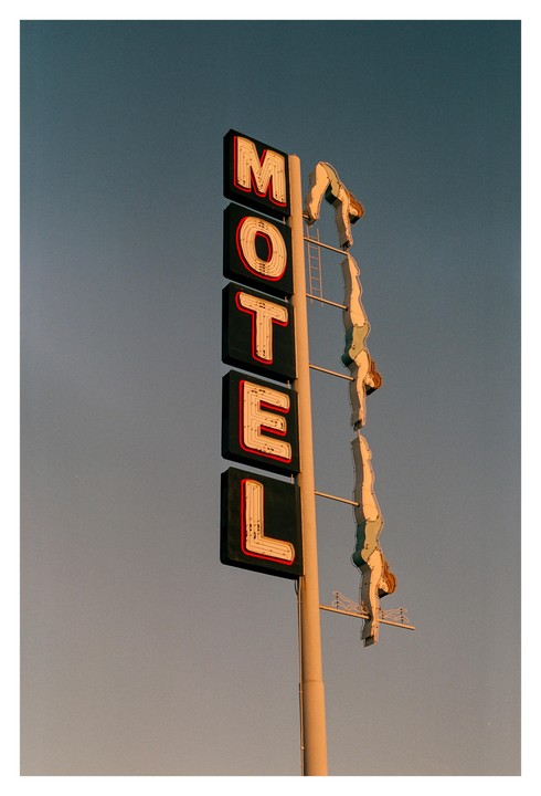 A neon motel sign with a diving woman is set against a clear sky.