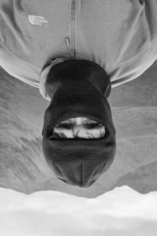 A man wearing a balaclava and jacket is shown upside down with mountains in the background.