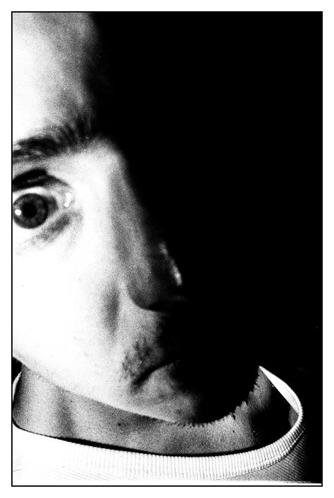 A man's face is partially illuminated in a high-contrast black and white portrait.
