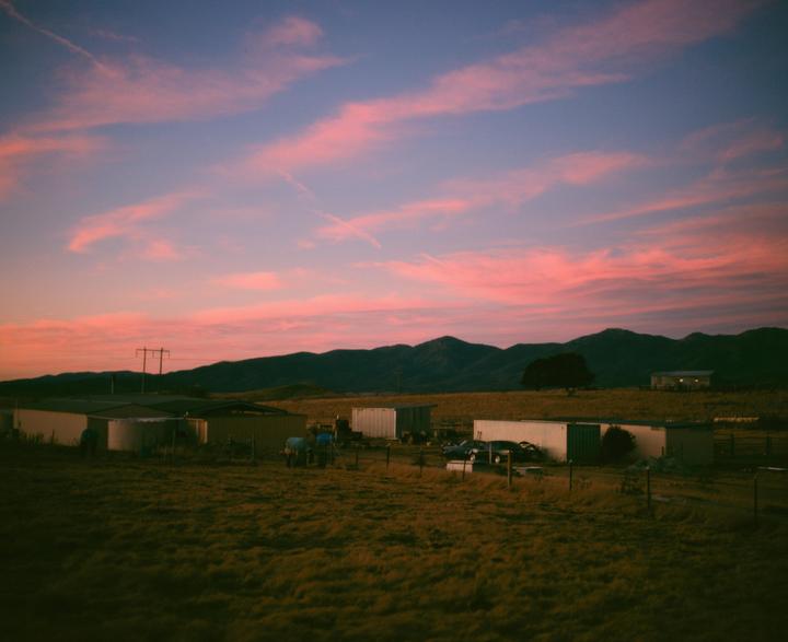 A rural landscape with buildings and mountains is visible under a sky with pink clouds.