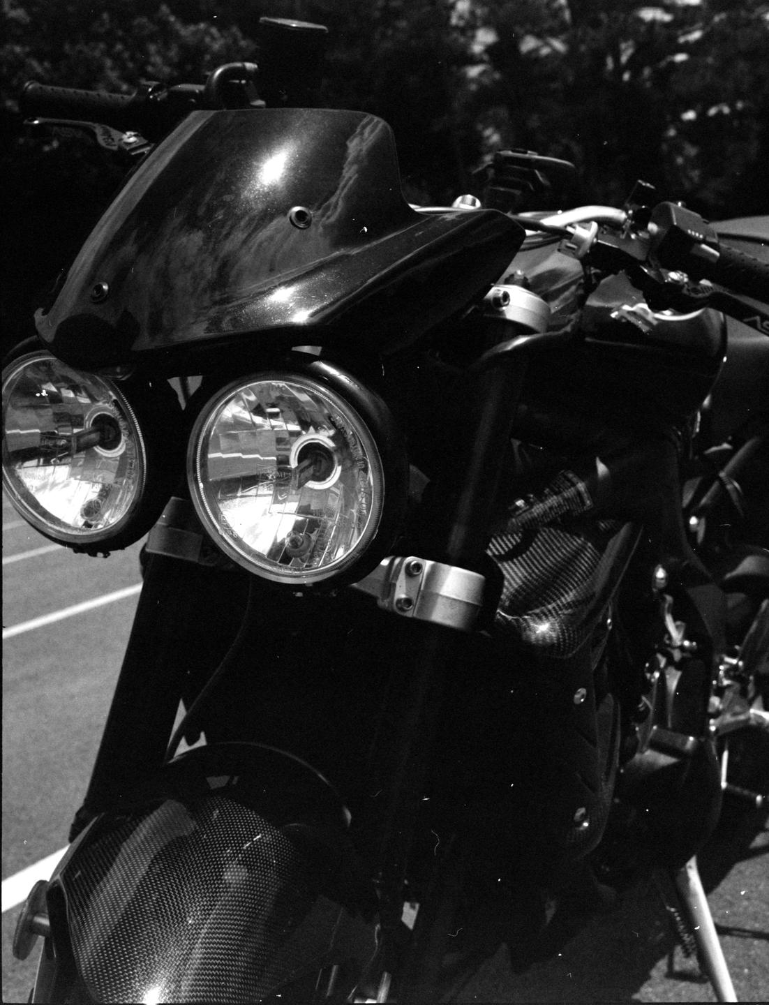 A black and white close-up shows the front of a motorcycle with two headlights and a small windshield.