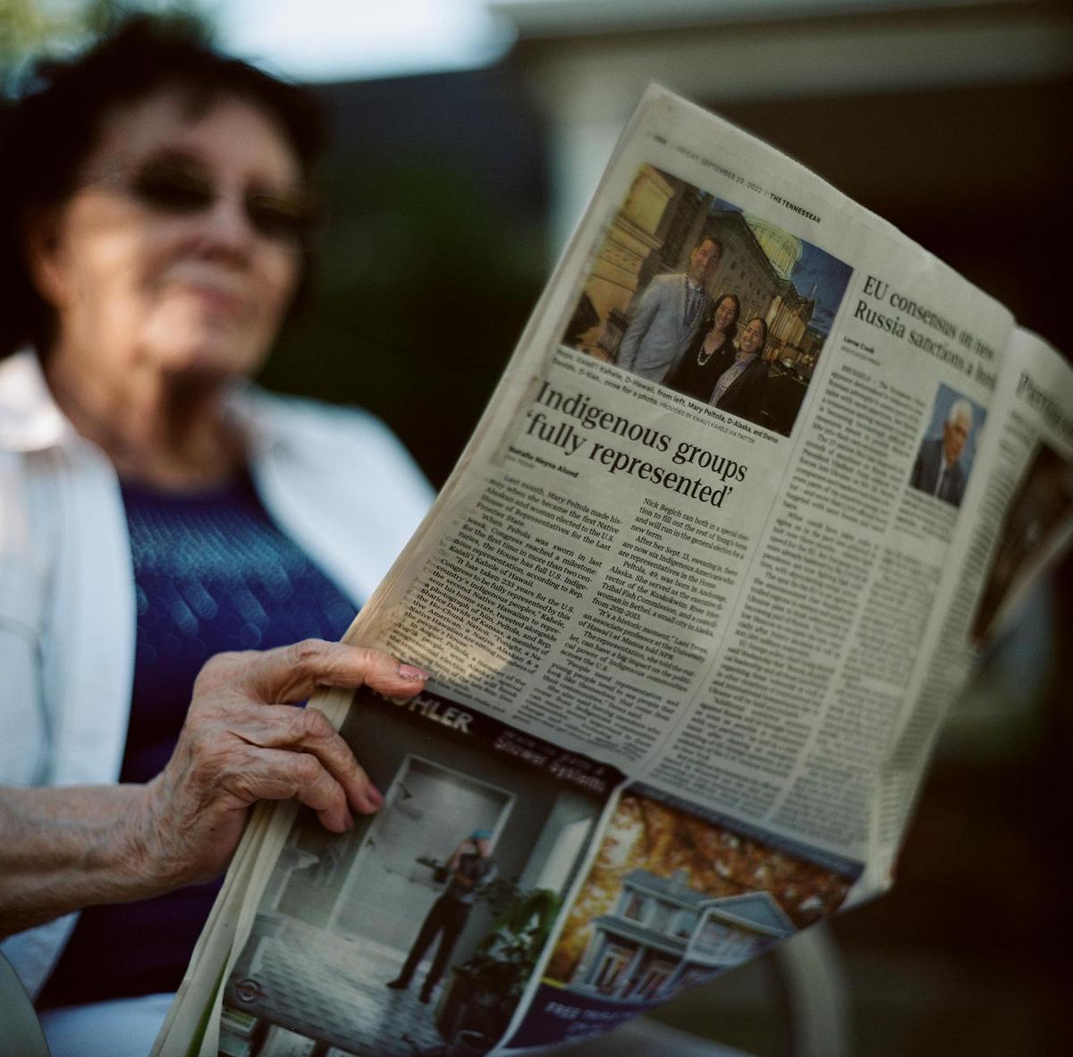 A woman holds a newspaper with the headline "Indigenous groups 'fully represented'" while sitting outdoors.